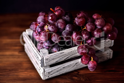 Branch of a dark grapes in a white box on a wooden background