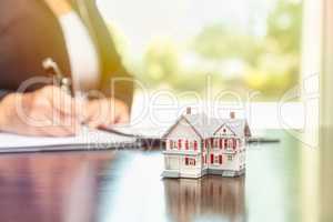 Woman signing real estate contract papers with small model home