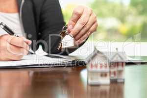 Woman signing real estate contract papers holding house keys and