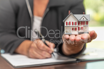 Woman signing real estate contract papers holding small model ho