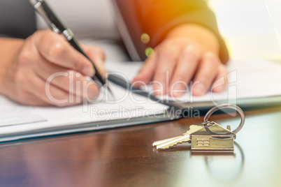 Woman signing real estate contract papers with house keys and ho
