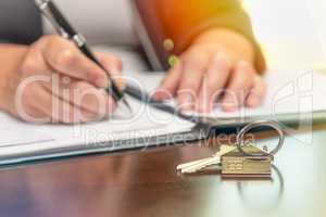 Woman signing real estate contract papers with house keys and ho