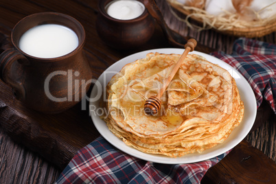 A stack of thin pancakes with honey on a wooden board.