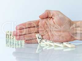 Hand stopping domino effect on white background.