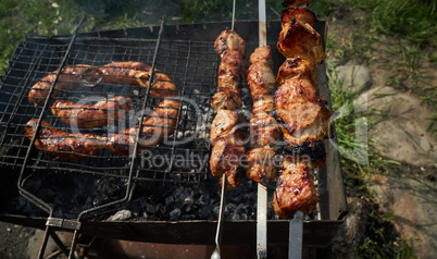Barbeque meat and sausages or bratwurst on a grill grate in backyard. Man preparing shashlik or shish kebab over charcoal. Grilled meat on metal skewer outdoor. BBQ party or picnic food. Close up shot