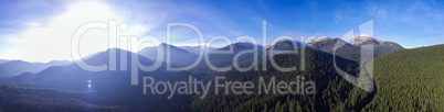 Bright sun rising over the mountains. Panorama of mountain landscape and dense forest from aerial view
