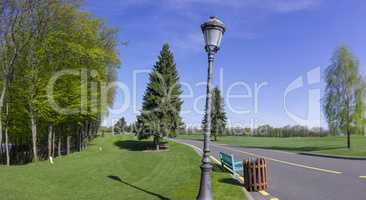 Night lantern by the road through the park, clear blue sky and green lawn with lawn grass.