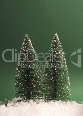 Two fir trees with snow on a green paper background, space for t