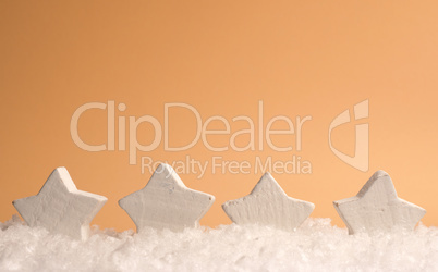Four white wooden star shapes with snow on an orange paper backg