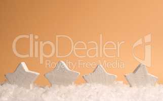 Four white wooden star shapes with snow on an orange paper backg