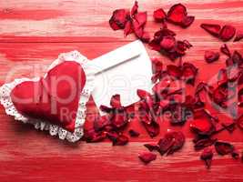 Red fabric heart with a letter and rose petals on wood