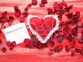 Red fabric heart with a letter and rose petals on wood