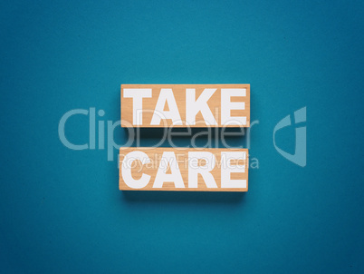 Two wooden blocks with inscription TAKE CARE on a blue backgroun