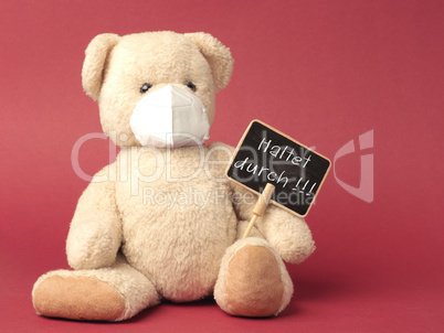 German Hold on, Teddy bear with protective mask holds sign