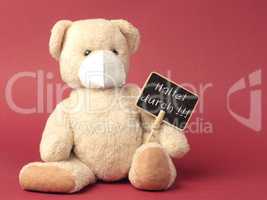 German Hold on, Teddy bear with protective mask holds sign