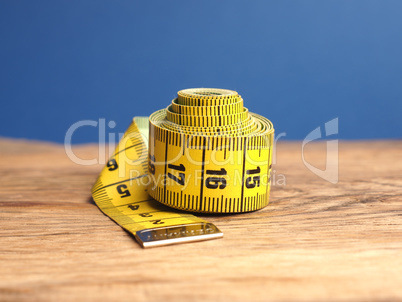 Yellow tailor tape measure on a wooden table, close up