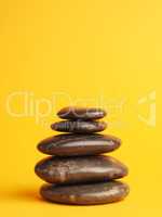 Five stacked dark massage stones on yellow