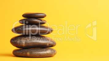 Five stacked dark massage stones on yellow