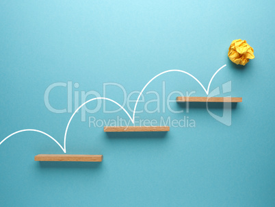 Yellow crumpled paper ball bounces up stairs on a blue backgroun
