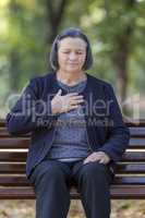 Senior lady clutching her chest in pain in park on an autumn day