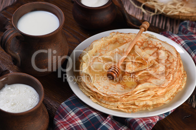 A stack of thin pancakes with honey on a wooden board.