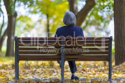 Aged woman sitting on bench in autumn park