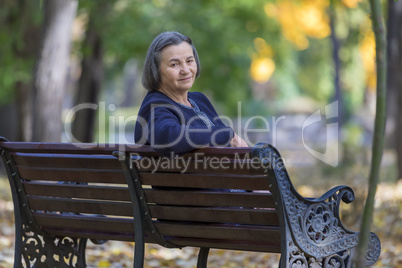 Aged woman sitting on bench in autumn park