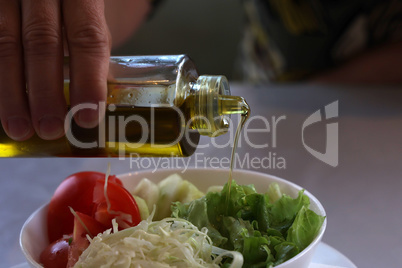 Pour olive oil on fresh lettuce with tomatoes, cucumber and herbs
