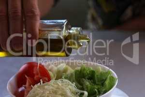 Pour olive oil on fresh lettuce with tomatoes, cucumber and herbs