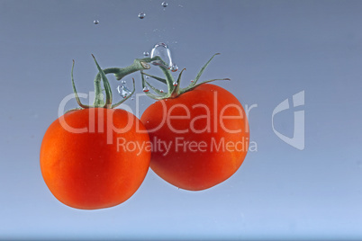 Close up of fresh and healthy cherry tomatoes falling into clear water