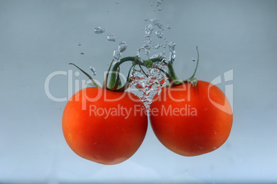 Close up of fresh and healthy cherry tomatoes falling into clear water