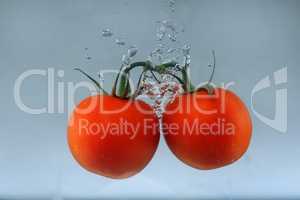 Close up of fresh and healthy cherry tomatoes falling into clear water