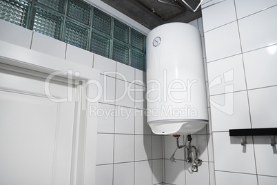 Modern gas tanked boiler in bathroom. Household budget water heater hanging on the wall in boiler room. ?ommon electric storage tank water heater. Home heating system in front of white tiled wall