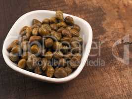 Organic capers in a white bowl on a rustic kitchen table