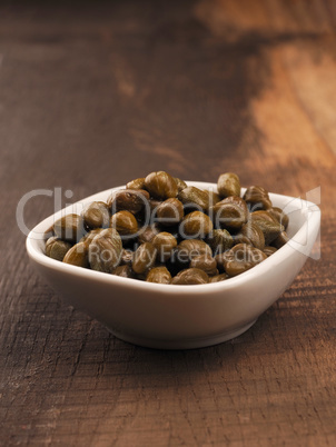Organic capers in a white bowl on a rustic kitchen table