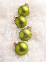 Four green Christmas baubles in the snow