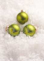 Three green Christmas baubles in the snow