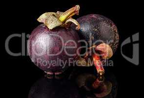 Two ripe mangosteen one after another on a black