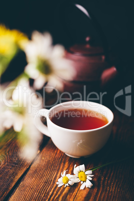 Cup of black tea and two chamomile flowers