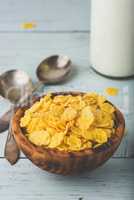 Bowl of corn flakes with spoons and bottle of milk
