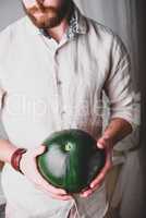 Bearded man in shirt holds in hands green watermelon