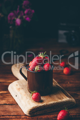 Fresh red strawberries in metal mug on table.