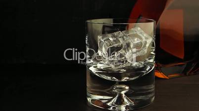 Pouring a scotch whisky in a glass with ice cubes, slow motion