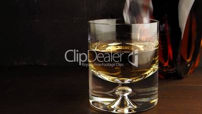 Pouring a scotch whisky in a glass with ice cubes, slow motion