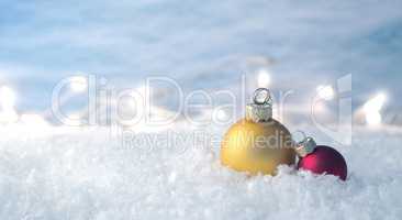 Two vintage Christmas baubles in snow with blurry Christmas ligh