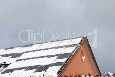 The tiled roof of the house with solar panels is covered with snow in winter