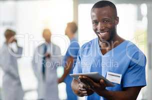 Staying current is an important part of my job. Portrait of a young doctor using a digital tablet with his colleagues in the background.