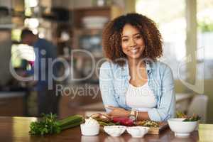 We like to keep our meals healthy. Portrait of a happy young woman preparing a healthy meal at home with her husband in the background.