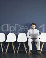 Last minute research before the interview. Studio shot of a young businessman using a laptop while waiting in line against a gray background.