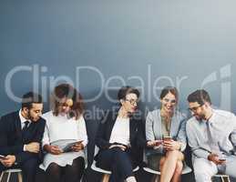 Nothing brings people together like technology. Studio shot of a group of businesspeople using wireless technology while waiting in line against a gray background.